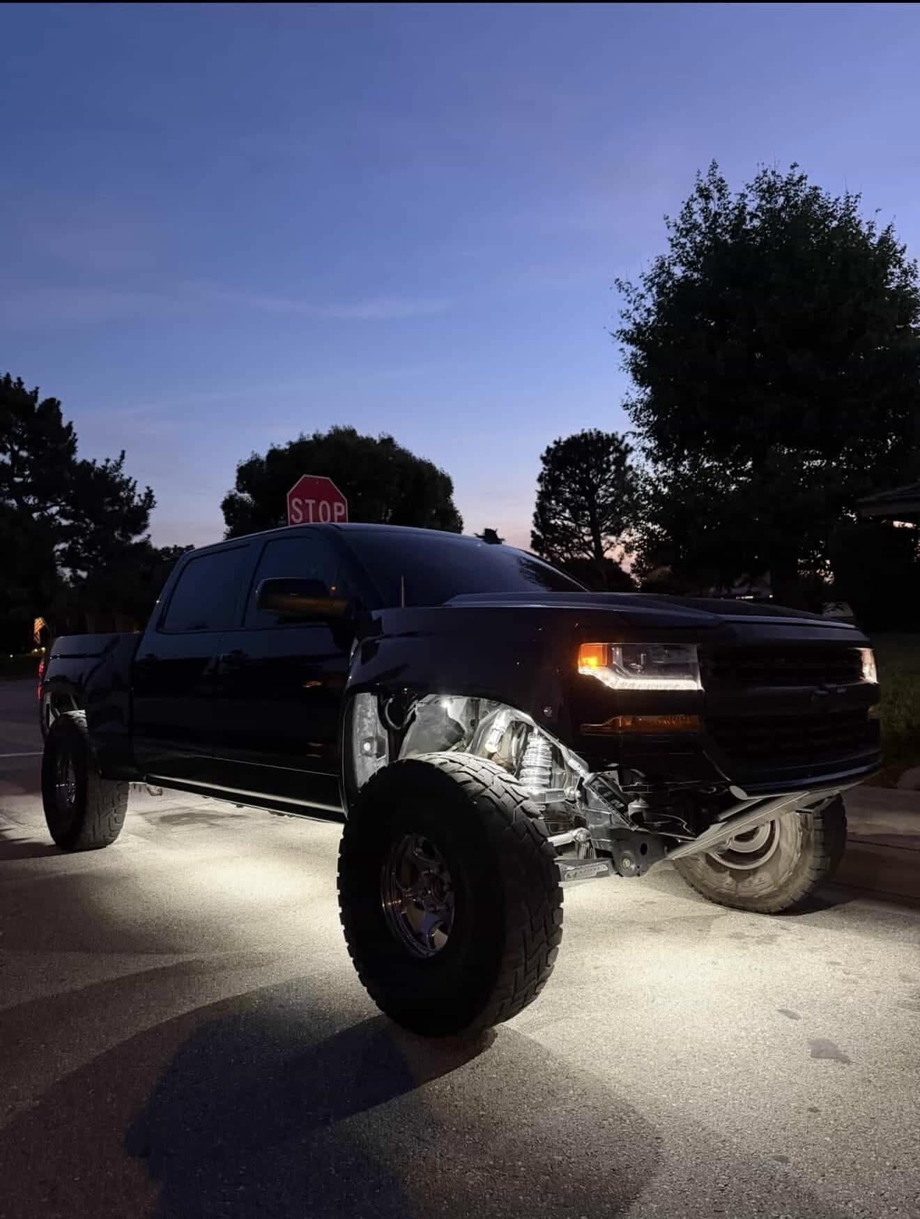 Lifted Silverado at dusk with white rock light underglow