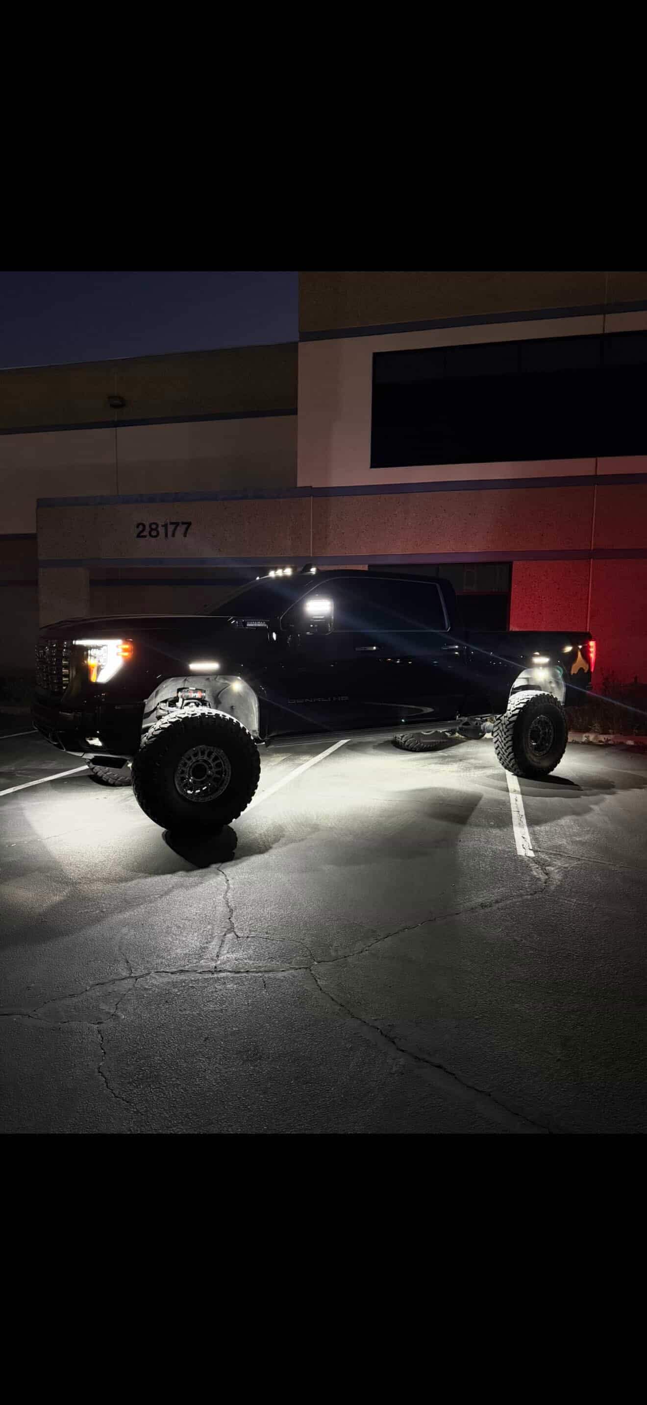 Black GMC Denali HD with rock lights at industrial complex